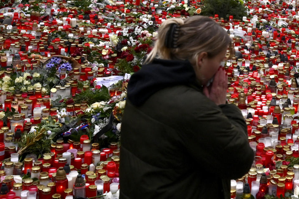 A young woman reacts by the floral tributes and candles left outside the headquarters of Charles University in downtown Prague, Czech Republic, Saturday, Dec. 23, 2023. A lone gunman opened fire at a university on Thursday, killing over 12 people and injuring dozens. (AP Photo/Denes Erdos)