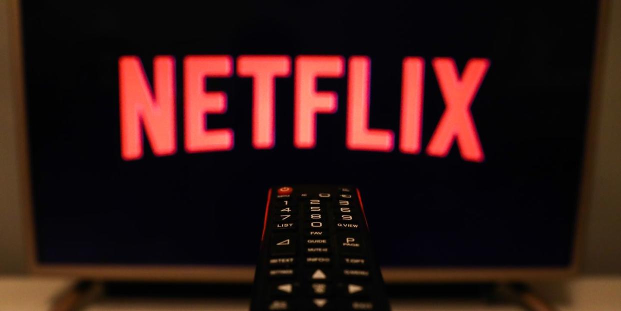 netflix in red against a black background with a remote control in the center of the foreground