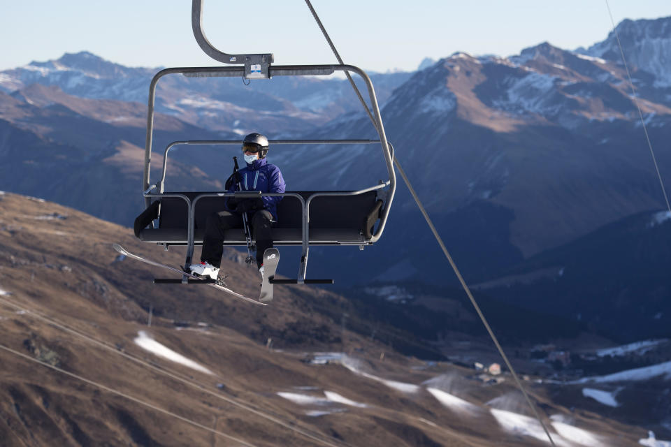 FILE - In this Sunday, Nov. 29, 2020 file photo a ski enthusiast wearing a protective face mask takes a chair lift in Arosa, Switzerland. Swiss ski stations that has become an epicenter of discord among Alpine neighbors. EU member states Austria, France, Germany and Italy are shutting or severely restricting access to the slopes this holiday season amid COVID-19 concerns, Switzerland is not. (Gian Ehrenzeller/Keystone via AP, File)