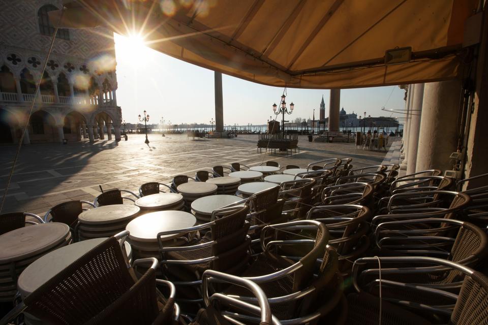 FILE - In this Monday, April 6, 2020 file photo, chairs and tables are piled in front of a bar in St. Mark's Square, in Venice during a lockdown to prevent the spread of the coronavirus. Businesses across Europe, many with employees on temporary unemployment due to coronavirus restrictions, are waiting for government rules to ease before some can go back to work. (AP Photo/Andrew Medichini, File)