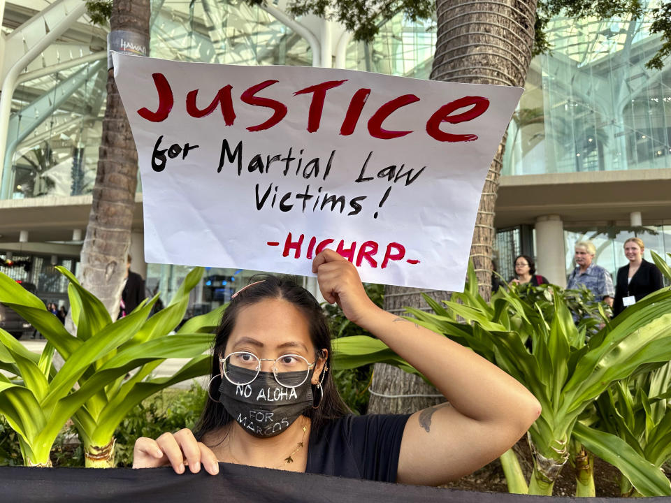 Protester Ia Maranon holds a sign outside the Hawaii Convention Center in Honolulu on Saturday, Nov. 18, 2023, to protest a visit by Philippines President Ferdinand Marcos Jr. and recall the actions taken by his late dictator father, Ferdinand Marcos Sr. The younger Marcos and current president was in Honolulu for a whirlwind trip on the way home from the Asia-Pacific Economic Cooperation summit in San Francisco to emphasize U.S.-Philippines relations and meet with Filipino community members in Hawaii. (AP Photo/Jennifer Kelleher)
