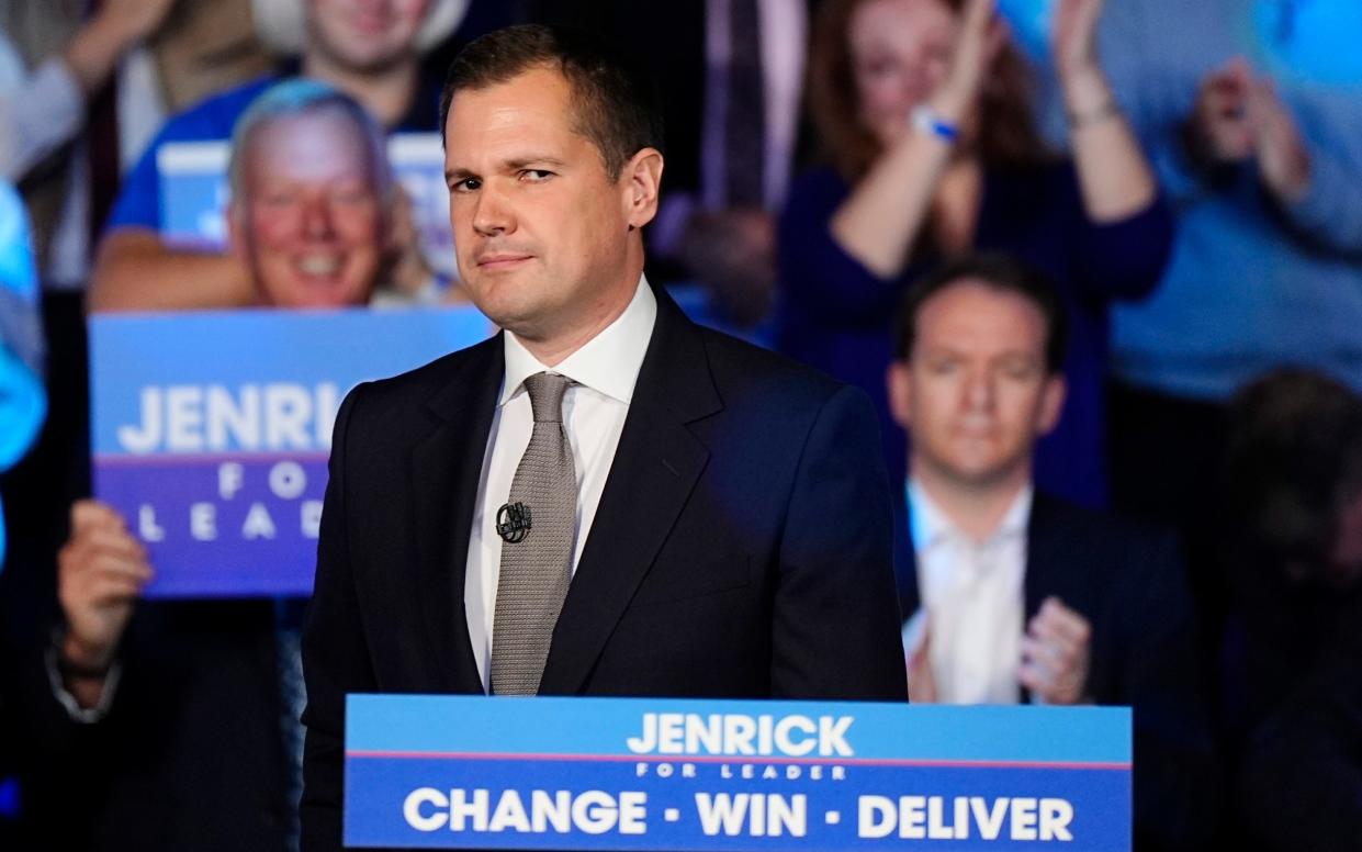 Mr Jenrick stands behind a lectern labelled 'Jenrick - Change - Win - Deliver'