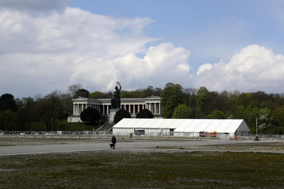 A woman and her dog walk by the 'Oktoberfest' beer festival area 'Theresienwiese' in front of the Bavaria statue and a corona test centre in Munich, Germany, Monday, May 3, 2021. The world's largest beer festival 'Oktoberfest' was cancelled last year due to the coronavirus outbreak. (AP Photo/Matthias Schrader)