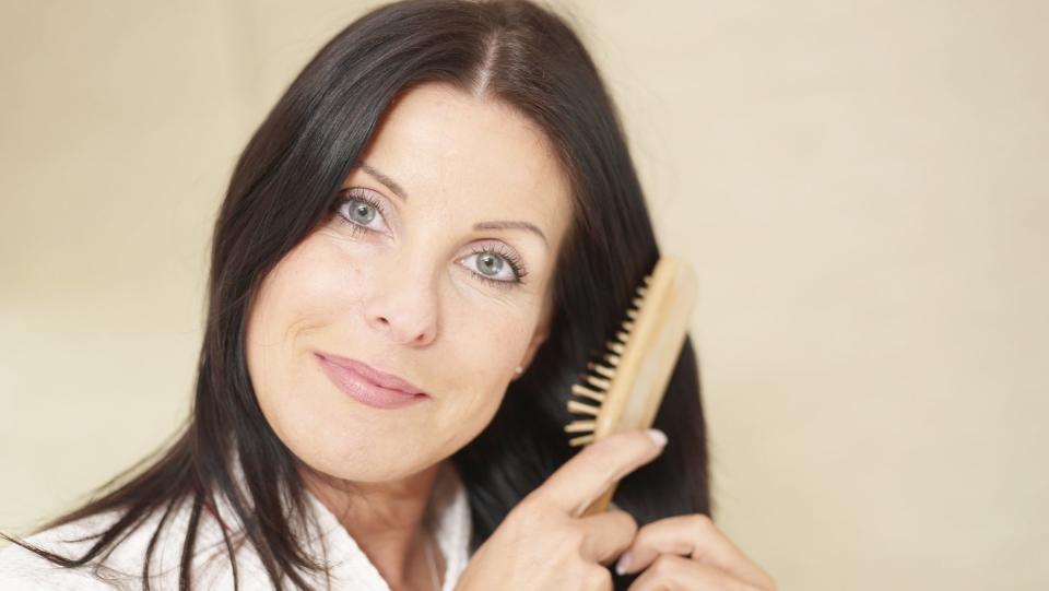 Mature woman brushing shiny, healthy hair.