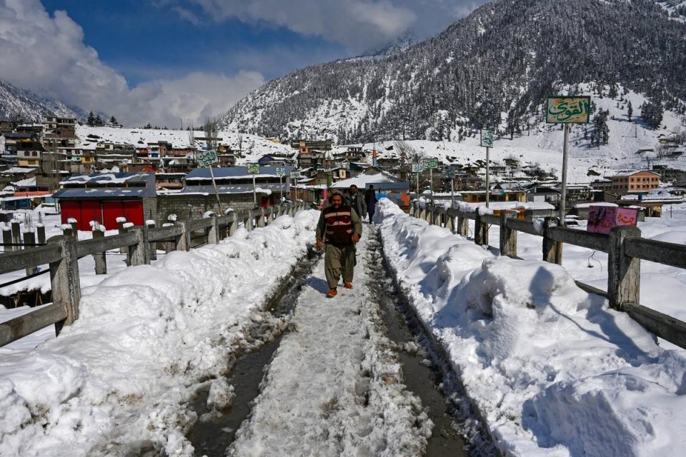 Tourists walk down a snow laden street in Kalam on 4 March 2024 (AFP via Getty Images)