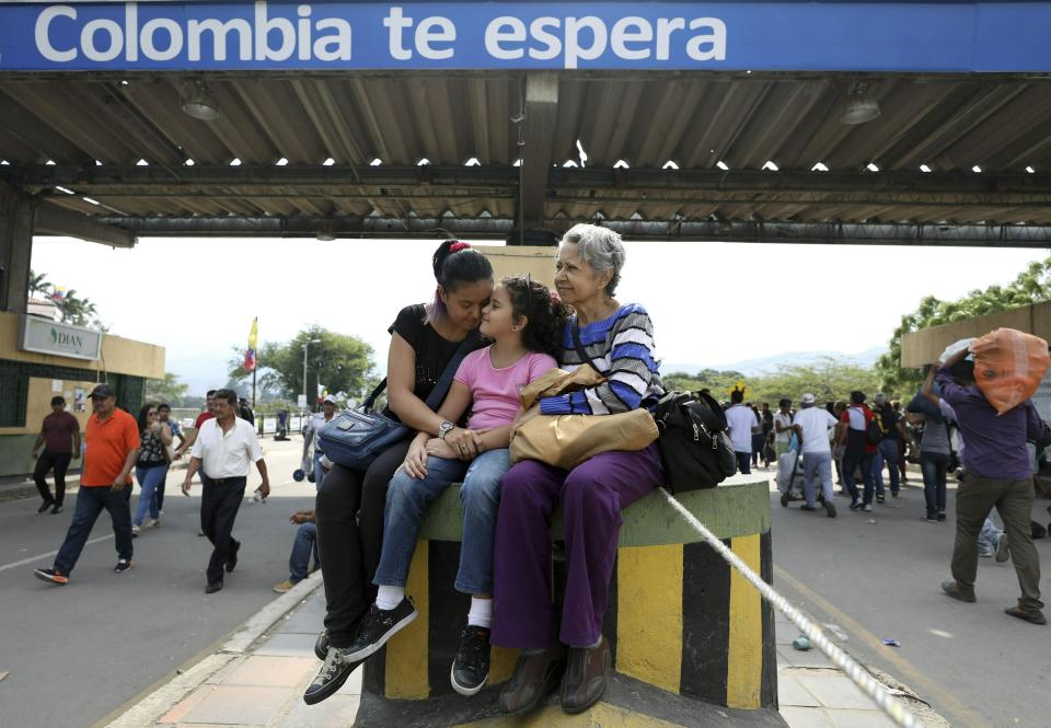 In this Feb. 11, 2019 photo, Venezuelan Diomira Becerra, left, sits with her 7-year-old daughter Hillary and her mother Betty Guerrero, during an interview at the entrance of the Simon Bolivar International Bridge, in La Parada, Colombia, near Cucuta. Becerra, who can see the Venezuelan mountains from her new home in Cucuta, said her young daughter Hillary often asks when they can go back. She was 4 when they left. (AP Photo/Fernando Vergara)