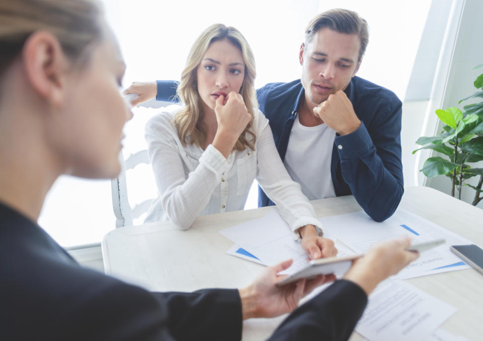 Real estate agent going through diocuments with concerned-looking couple.