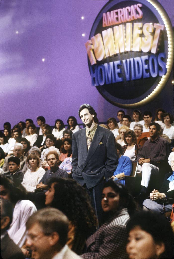 Bob stands in the middle of an audience in front of the show's logo