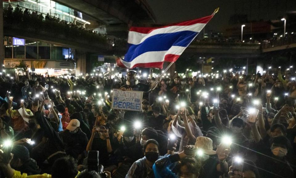 Protesters wave the Thai national flag and shine their phone lights in Bangkok