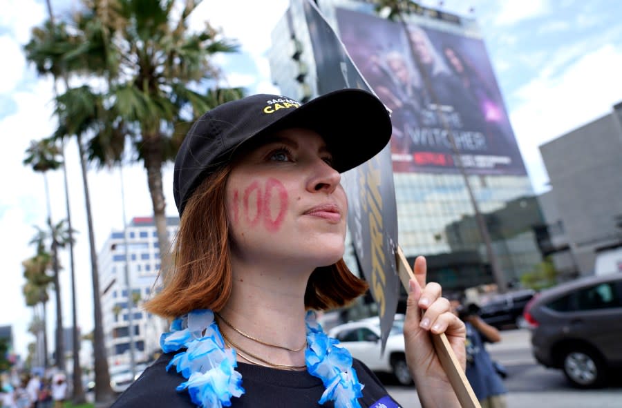 SAG-AFTRA member Emily Kincaid dons a 100 on her face as she carries a sign on a picket line outside Netflix studios on Wednesday, Aug. 9, 2023, in Los Angeles. The Hollywood writers strike reached the 100-day mark today as the U.S. film and television industries remain paralyzed by dual actors and screenwriters strikes. (AP Photo/Chris Pizzello)