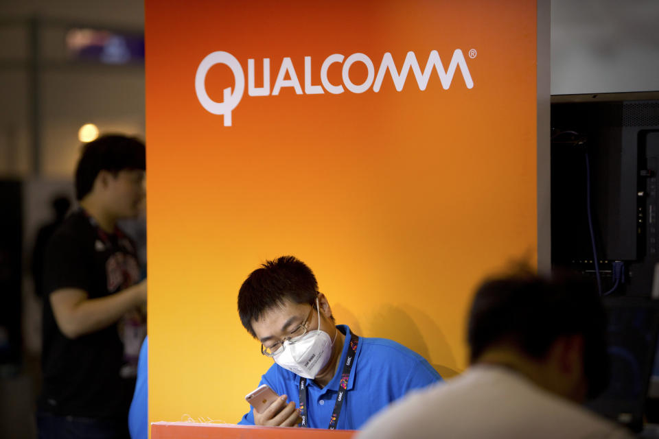 FILE - In this Wednesday, April 29, 2015, file photo, an employee wearing a face mask checks his cellphone at a display booth for Qualcomm at the Global Mobile Internet Conference in Beijing. Apple is intensifying its legal battle with Qualcomm over the technology in iPhones and iPads as Apple seeks to void some of the chip maker’s patent claims and licensing agreements. Qualcomm has disputed Apple’s claims that Qualcomm is overcharging for patent-related license fees on iPhone and iPad sales. Apple says that a recent Supreme Court ruling strengthens its argument that Qualcomm cannot continue to demand royalties for patents after selling its cellular chips. (AP Photo/Mark Schiefelbein, File)