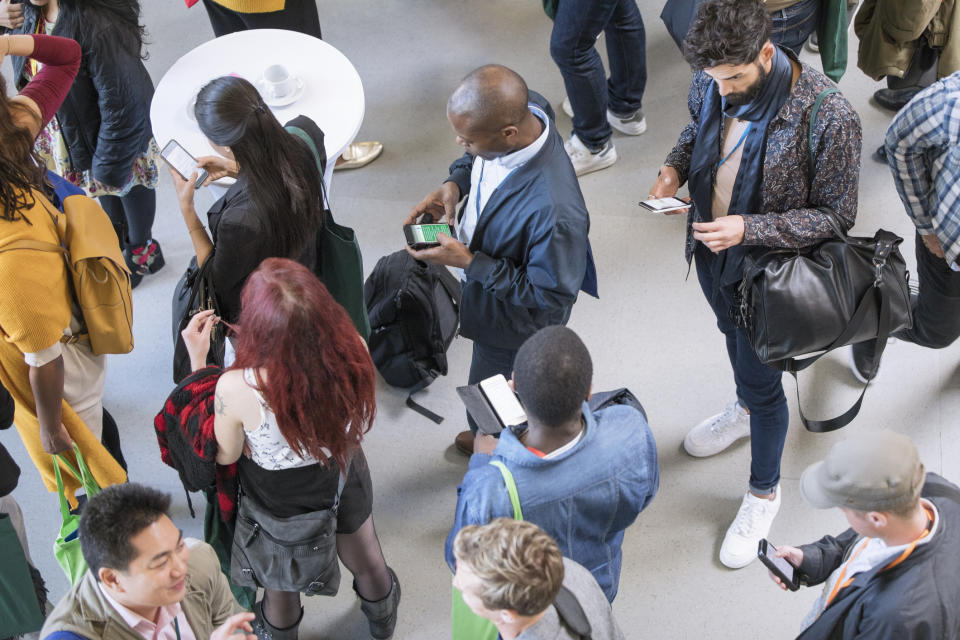 Photos of people standing at a conference on their phones.