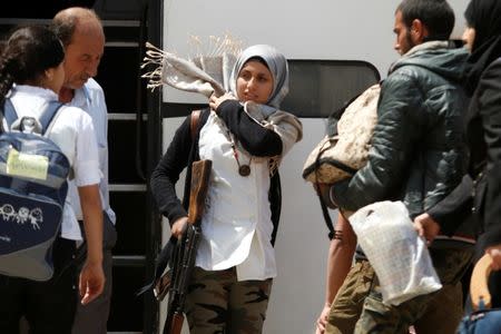 A rebel woman fighter fixes her headscarf as she carries her weapon before boarding a bus, as rebel fighters and their families evacuate the besieged Waer district, after an agreement was reached between rebels and Syria's army, in Homs, Syria May 20, 2017. REUTERS/Omar Sanadiki