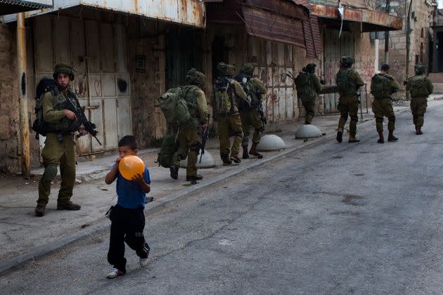 Un ni&#xf1;o palestino infla un globo delante de soldados israel&#xed;es de patrulla por Hebr&#xf3;n, Cisjordania.&#xa0; (Photo: Bernat Armangue via AP)