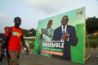 People walk pass next to a campaign billboard showing the candidats of the ruling coalition party, the Rally of Houphouetists for Democracy and Peace (RHDP) ahead of the legislative election in Abidjan