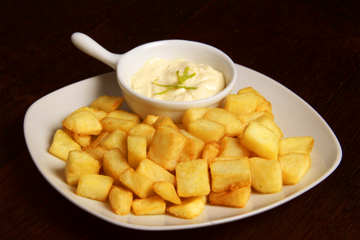 Papas bravas on a white plate with a side of mayonnaise sauce in a small bowl on a dark brown table