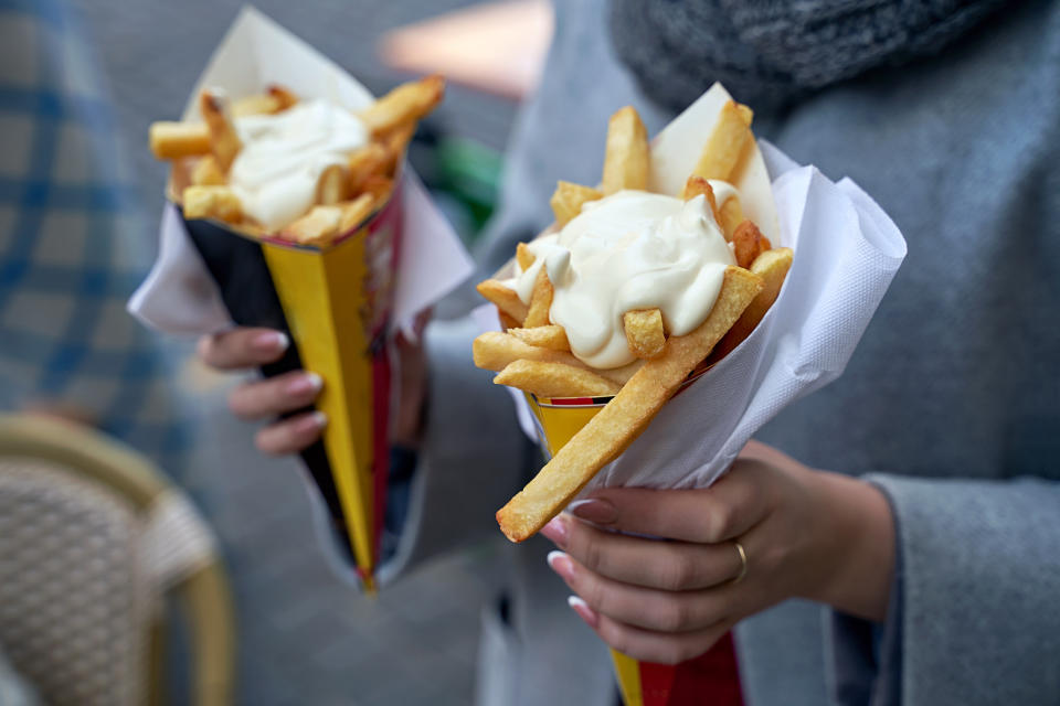 Two hands holding cones of French fries topped with mayonnaise
