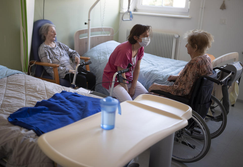 An activity leader interacts with residents inside a room at a nursing home in Ammerschwir, France Thursday April 16, 2020. The elderly make up a disproportional share of coronavirus victims globally, and that is especially true in nursing homes, which have seen a horrific number of deaths around the world. In France, nursing home deaths account for more than a third of the country's total coronavirus victims — figures the government now documents meticulously after weeks of pressure. (AP Photo/Jean-Francois Badias)