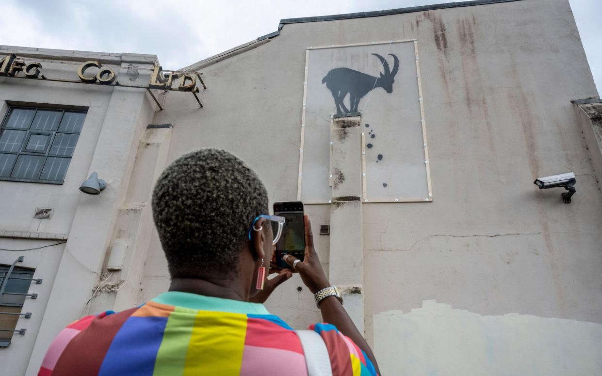 A woman views an artwork, now under protective perspex, by Banksy