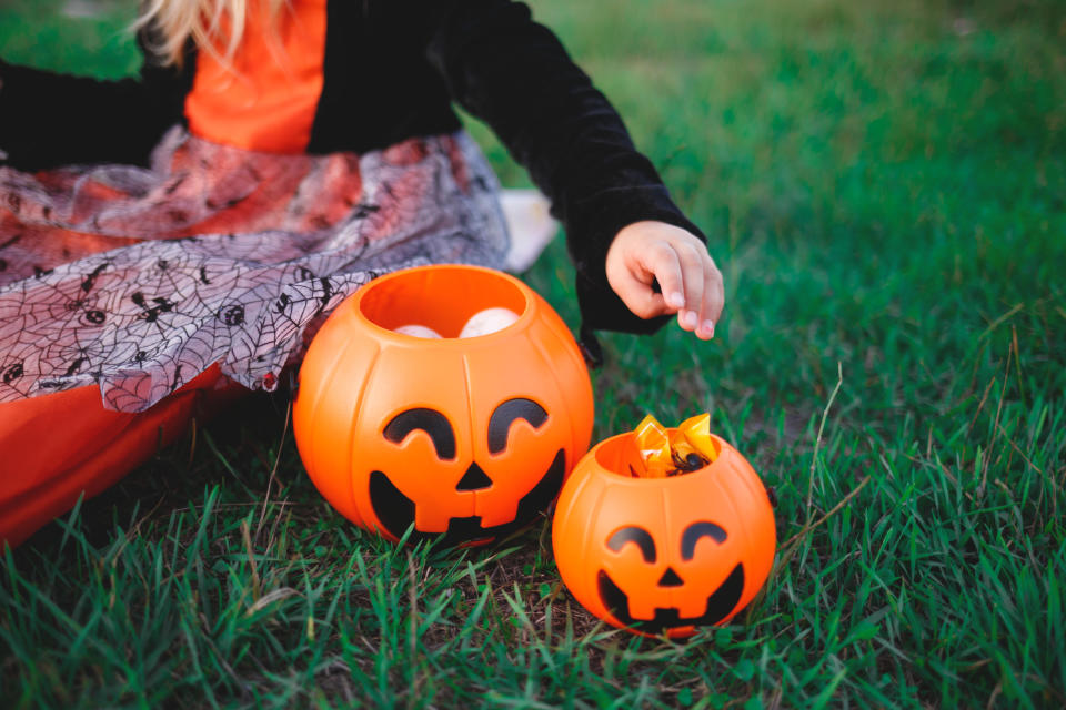 a child's hand reaches for candy in a pumpkin-shaped candy basket.