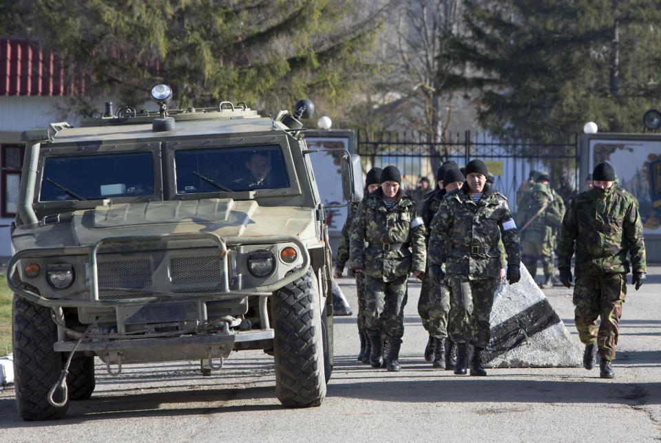 Ukrainian troops with white bands on their sleeves march past an unmarked Russian military vehicle outside a Ukrainian military base in Perevalne, Crimea, Ukraine, Monday, March 17, 2014. Crimea held a referendum Sunday, in which an overwhelming majority voted for breaking off from Ukraine and joining Russia. (AP Photo/Andrei Udovichenko)