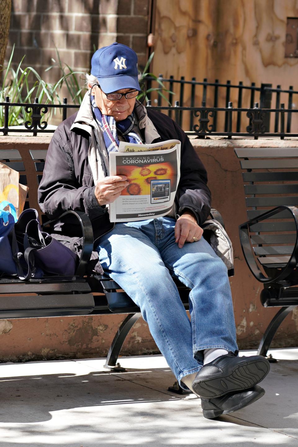 A man in New York sits on a bench reading a newspaper with 'Tracking the Coronavirus' visible on the page as the coronavirus continues to spread across the United States.