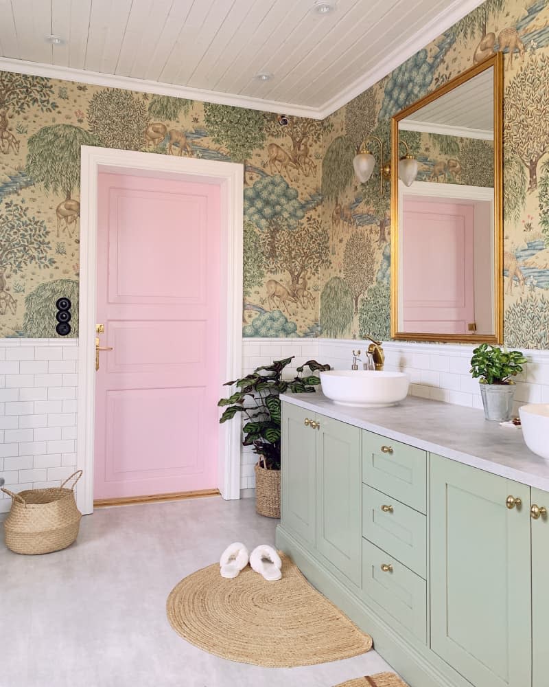 bathroom with green botanical wallpaper, pale sage green cabinets, and gold accents