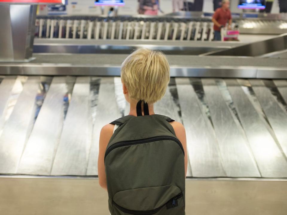 A child stands at the luggage conveyor belt in an airport.