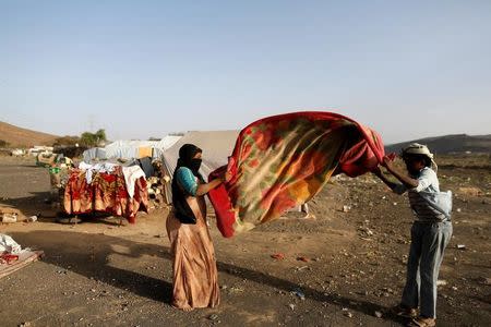 People shake a blanket to rid it of dust at a camp for people displaced by the war near Sanaa, Yemen April 24, 2017. REUTERS/Khaled Abdullah