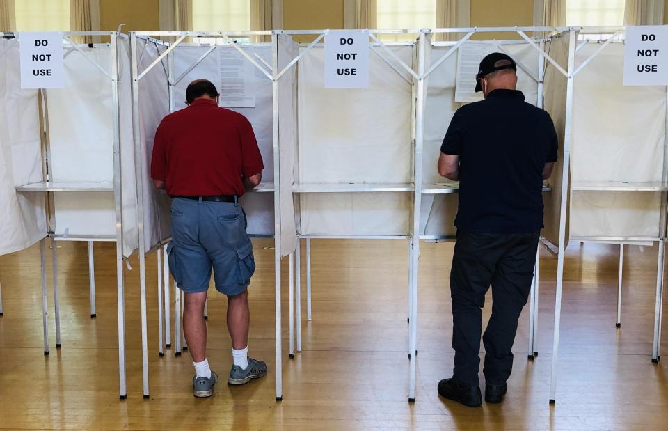 Timothy Connors, left, and Pete Donaher keep one empty booth between them as they vote in the auditorium at the Kennebunk Town Hall on Tuesday, July 14, 2020.
