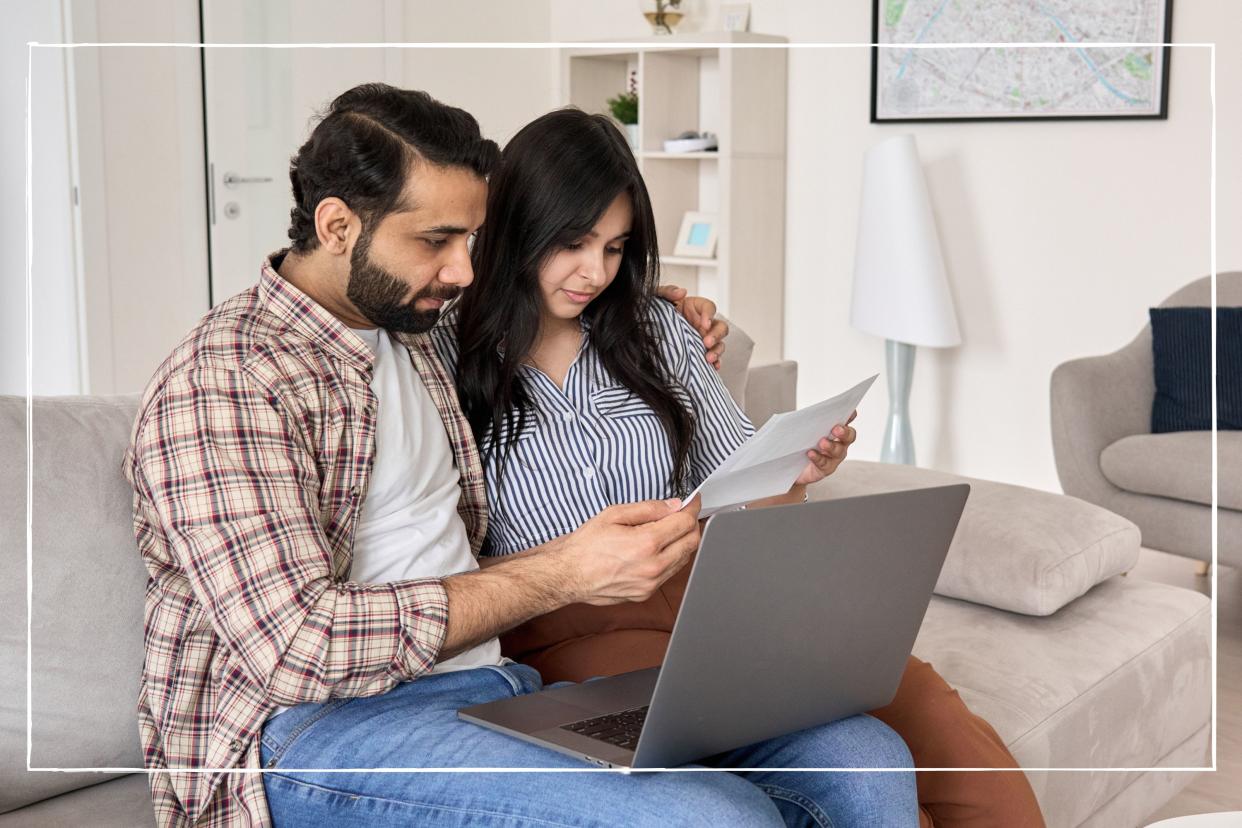  Couple sitting on sofa with laptop, looking at energy bills. 