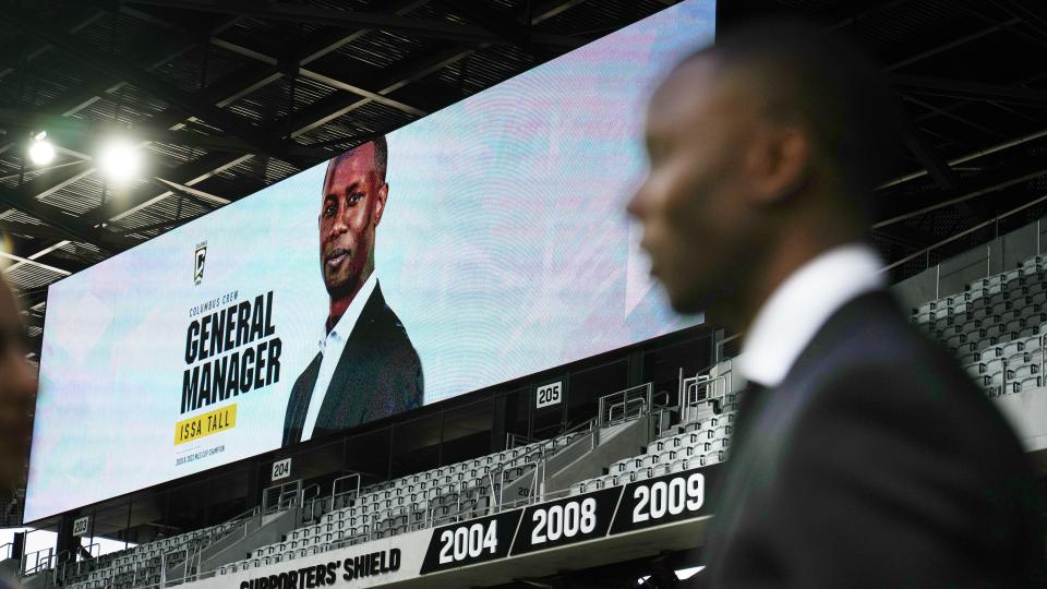 As his likeness is projected on a screen, new Crew general manager Issa Tall talks with a reporter at Lower.com Field on Friday.