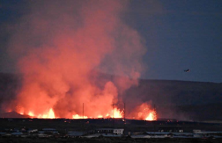 Un helicóptero vuela cerca de explosiones de lava y humo cerca de edificios residenciales en la ciudad suroccidental islandesa de Grindavik tras una erupción volcánica el 14 de enero de 2024. 