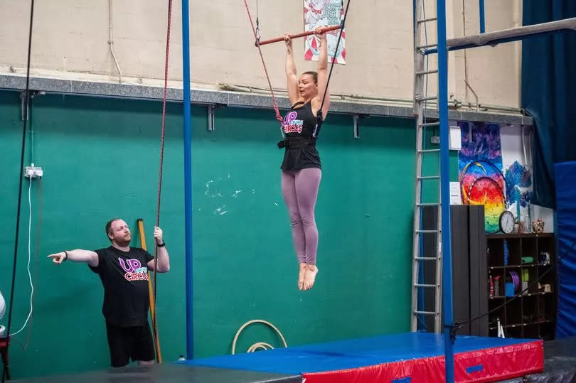 A woman is instructed as she hangs from the trapeze