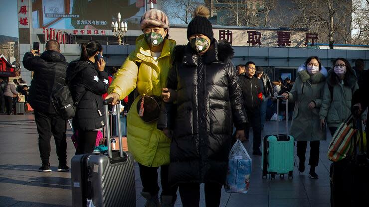 Reisende stehen mit Rollkoffern in der Nähe des Pekinger Bahnhofs und tragen Mundschutz. Die Menschen haben Angst vor einer landesweiten Ausbreitung des Virus. Foto: dpa