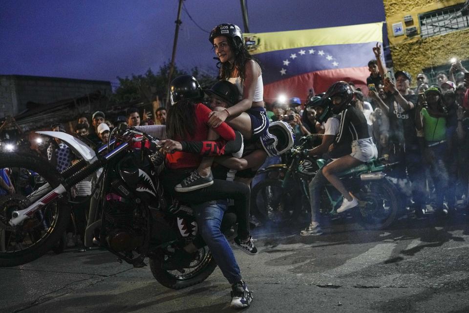 Un motociclista lleva tres mujeres mientras realiza un caballito con su motocicleta durante una exhibición en el barrio de Chapellin en Caracas, Venezuela, el 12 de junio de 2022. (AP Foto/Matias Delacroix)