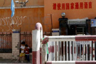 In this Aug. 31, 2018, photo, children play outside the entrance to a school ringed with barbed wire, security cameras and barricades near a sign which reads "Please use the nation's common language" indicating the use of Mandarin in Peyzawat, western China's Xinjiang region. Uighurs fear the Chinese government's expansion of compulsory Mandarin-intensive classes and boarding schools away from home will gradually erode their children's Central Asian ethnic identity and Islamic beliefs. (AP Photo/Ng Han Guan)