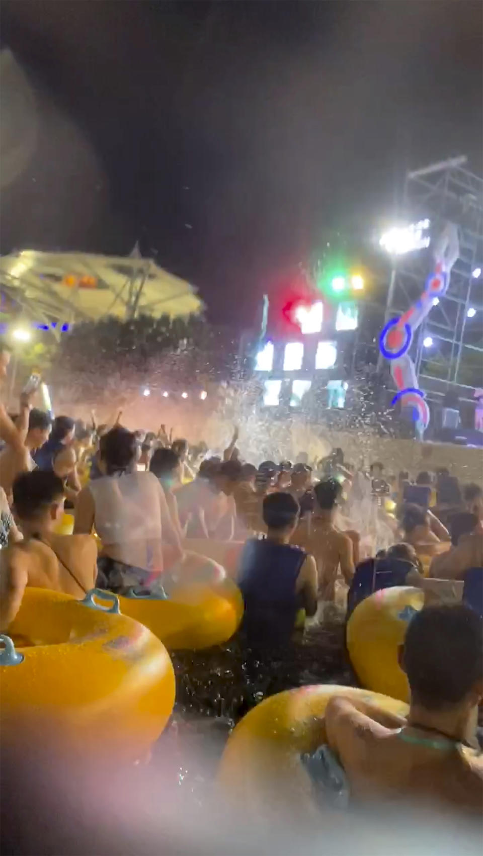 This image made from an Aug 3, 2020 video shows crowd gather in a pool as they watch performers on a stage at Wuhan Maya Beach Water Park in Wuhan, central China. For more than two months, the 11 million residents of Wuhan endured a strict lockdown as coronavirus raced around the city. Now, some are letting loose en masse at rocking nighttime pool parties at the popular amusement park chain. The park reopened in late June, and the crowds have picked up in August. (anonymous photo via AP)