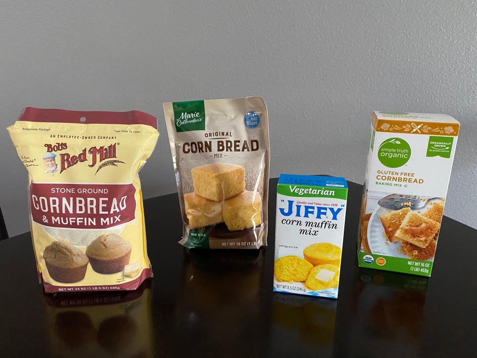 Four packages of cornbread from Bob's Red Mill, Marie Callender's, Jiffy, and Simple Truth Organic on black table