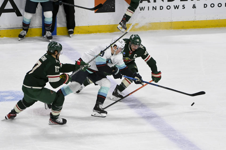Seattle Kraken center Ryan Donato, center, battles Minnesota Wild defenseman Jared Spurgeon, right, and left wing Marcus Foligno for control of the puck during the first period of an NHL hockey game Monday, March 27, 2023, in St. Paul, Minn. (AP Photo/Craig Lassig)
