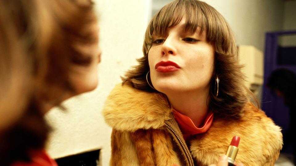 Woman looking in the mirror while applying red lipstick