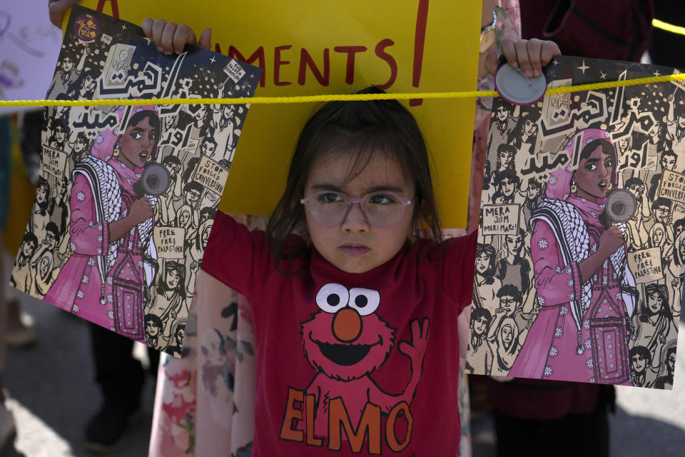 A girl displays posters as she stand beside her mother taking part in a rally called by socialist-feminist organisation 'Women Democratic Front' to mark International Women's Day, in Islamabad, Pakistan, Friday, March 8, 2024. The day officially recognised by the United Nations in 1977, is celebrated around the world on March 8. (AP Photo/Anjum Naveed)
