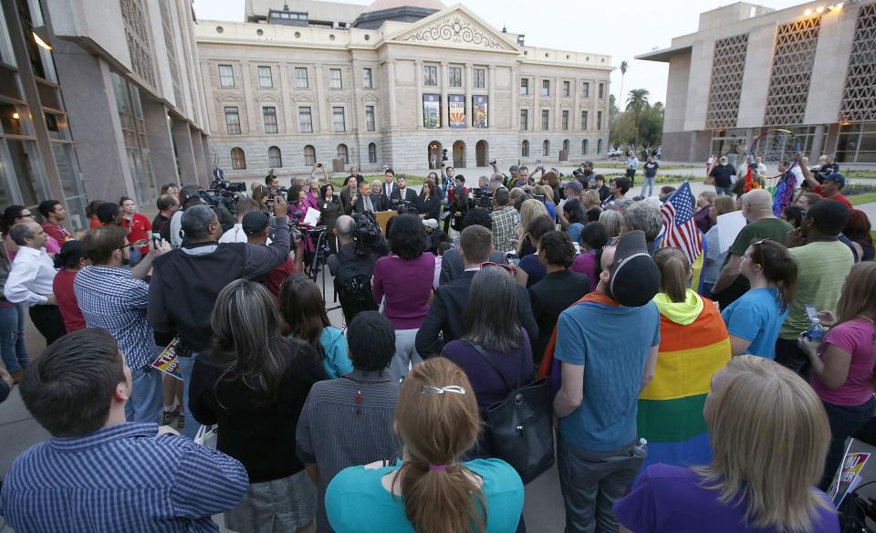 With the Arizona Capitol in the background and dozens of gay right supporters and members of the media surrounding them, Democratic representative Sen. Steve Gallardo, D-Phoenix, speaks at a podium about Arizona Gov. Jan Brewer's veto of SB1062, a bill designed to give added protection from lawsuits to people who assert their religious beliefs in refusing service to gays, at the Arizona Capitol on Wednesday, Feb. 26, 2014, in Phoenix. (AP Photo/Ross D. Franklin)
