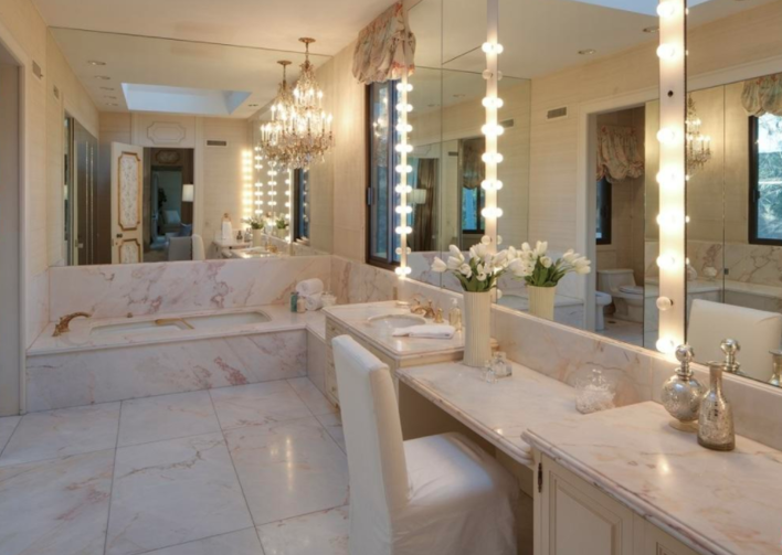 <p>The bathroom has marble flooring and vanities, with a bathtub and chandelier. This bathroom exudes opulence.</p>