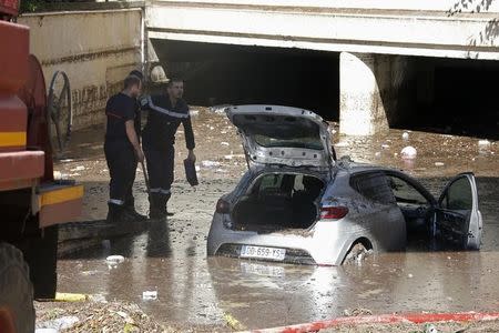 French fireman work near an abandoned car stuck in muddy waters near an underpass after flooding caused by torrential rain in Cannes, France, October 4, 2015. REUTERS/Eric Gaillard