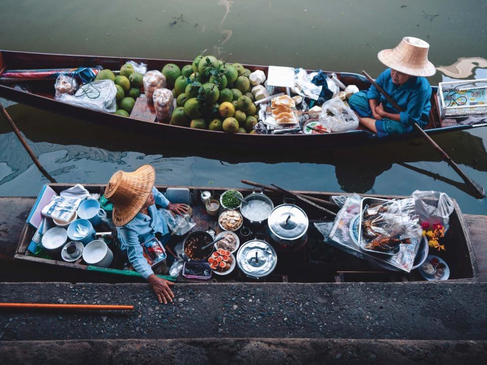 People sitting on boats near land selling food.