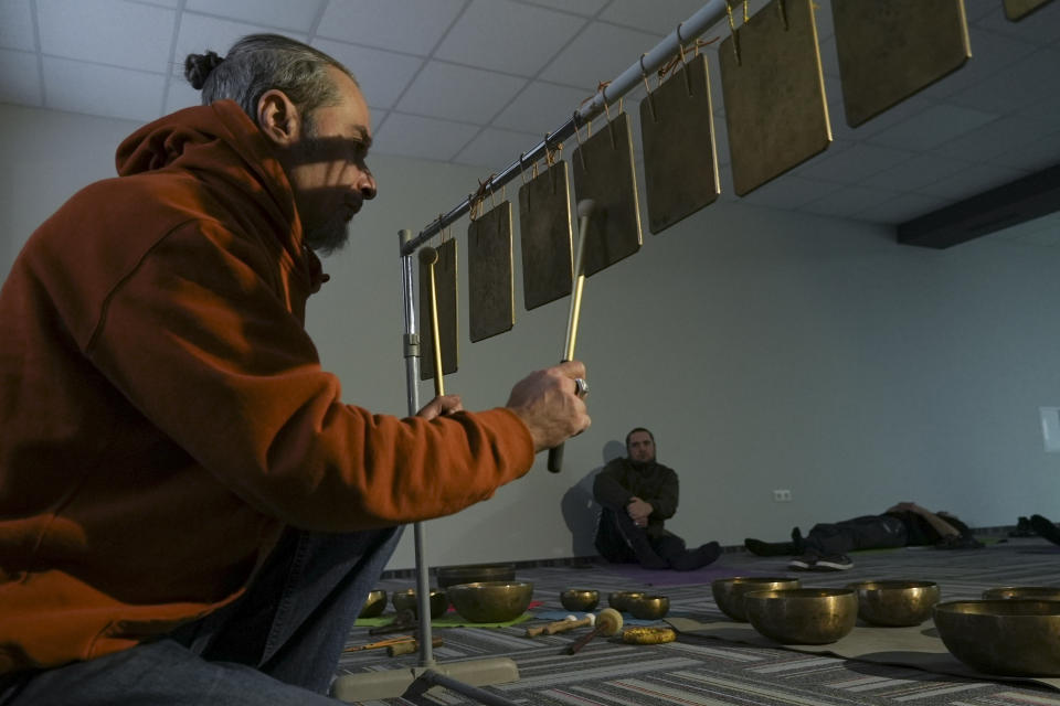 A man plays sounds as soldiers lie in a room at a clinic which treats veterans for PTSD, post-combat stress and post-concussion trauma, in Kyiv, Ukraine, Monday, Nov. 21, 2022. When peace returns to Ukraine, many thousands of its combatants will likely return with psychological scars from the battlefields. A mental health rehabilitation center for soldiers on the outskirts of Ukraine's capital, Kyiv, treats post-traumatic disorders with acupuncture, soothing sounds and other therapies. (AP Photo/John Leicester)