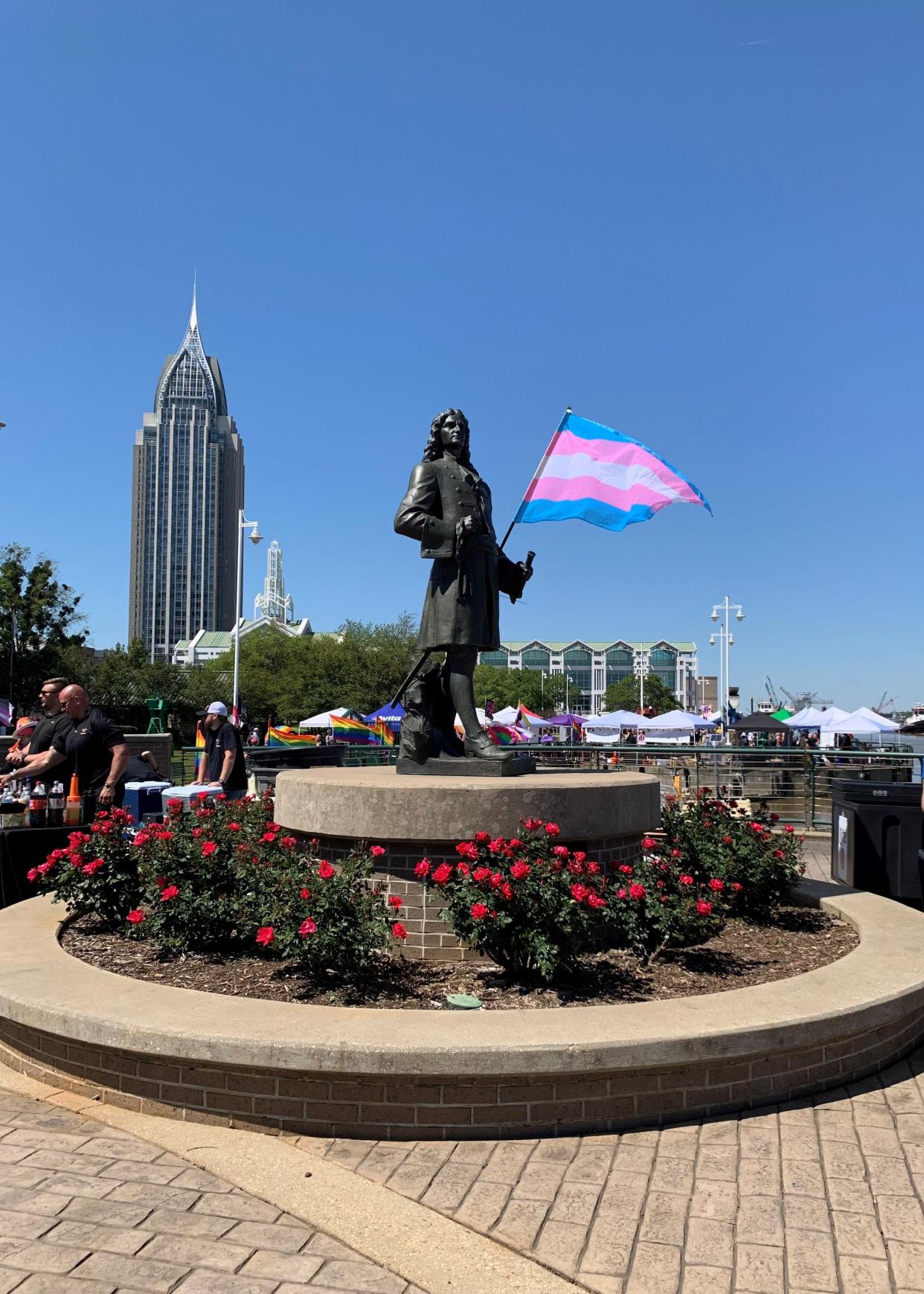 A transgender Pride flag unfurls in the wind during April's Pridefest in Mobile, Alabama. Booths and flags from the festival can be seen in the background.