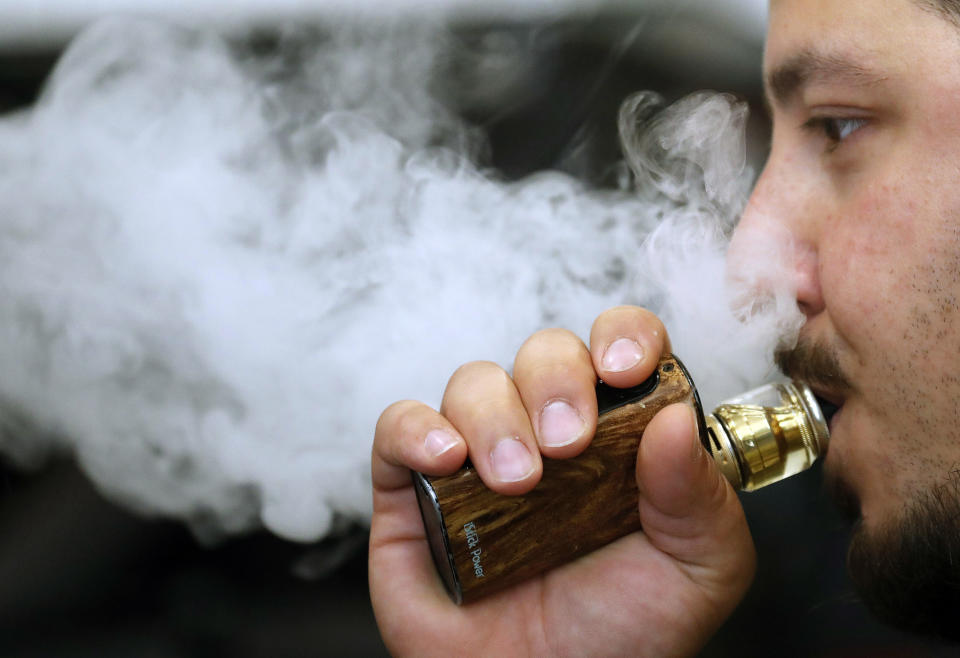 A man breathes vape from an e-cigarette at a vape shop in London, Friday, Aug. 17, 2018. A report by the British science and technology MPs committee suggest that rules around e-cigarettes should be relaxed to help accelerate already declining smoking rates. (AP Photo/Frank Augstein)
