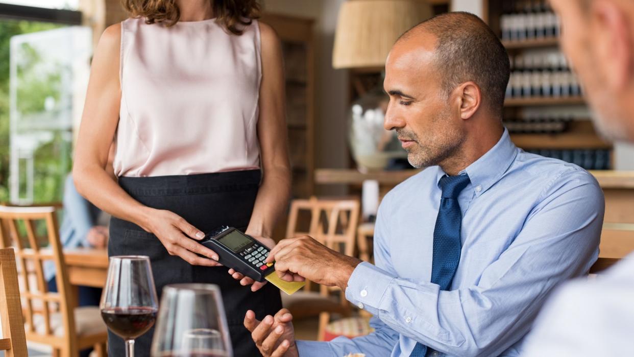 Waiter holding credit card swipe machine while customer typing code.